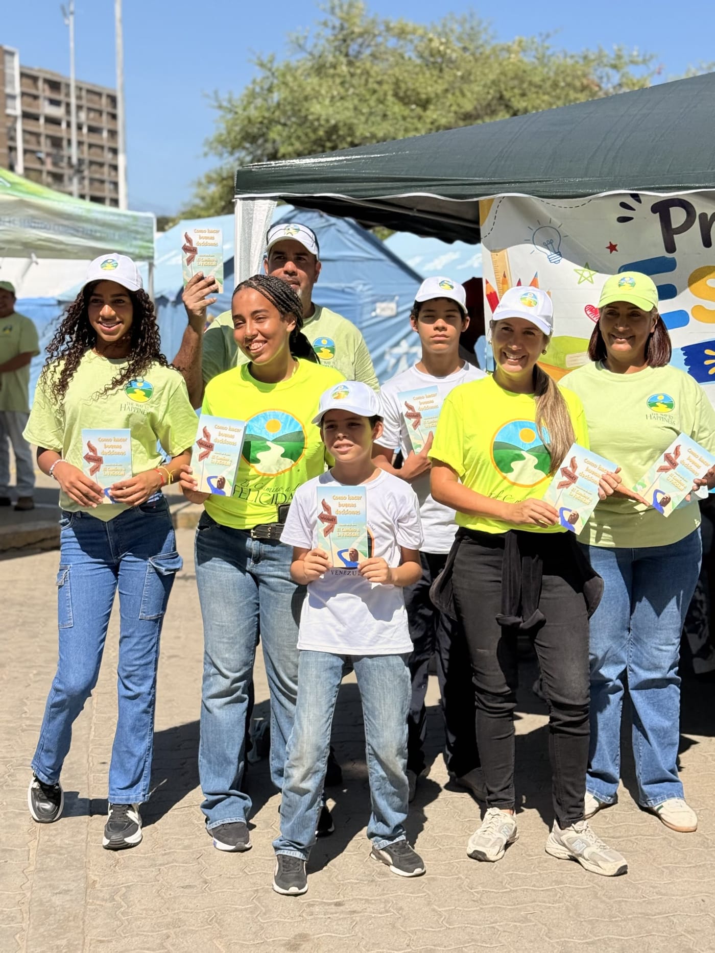 Voluntarios y niños con sus libritos de El Camino a la Felicidad frente a la carpa del Proyecto Escolar La Guaira
